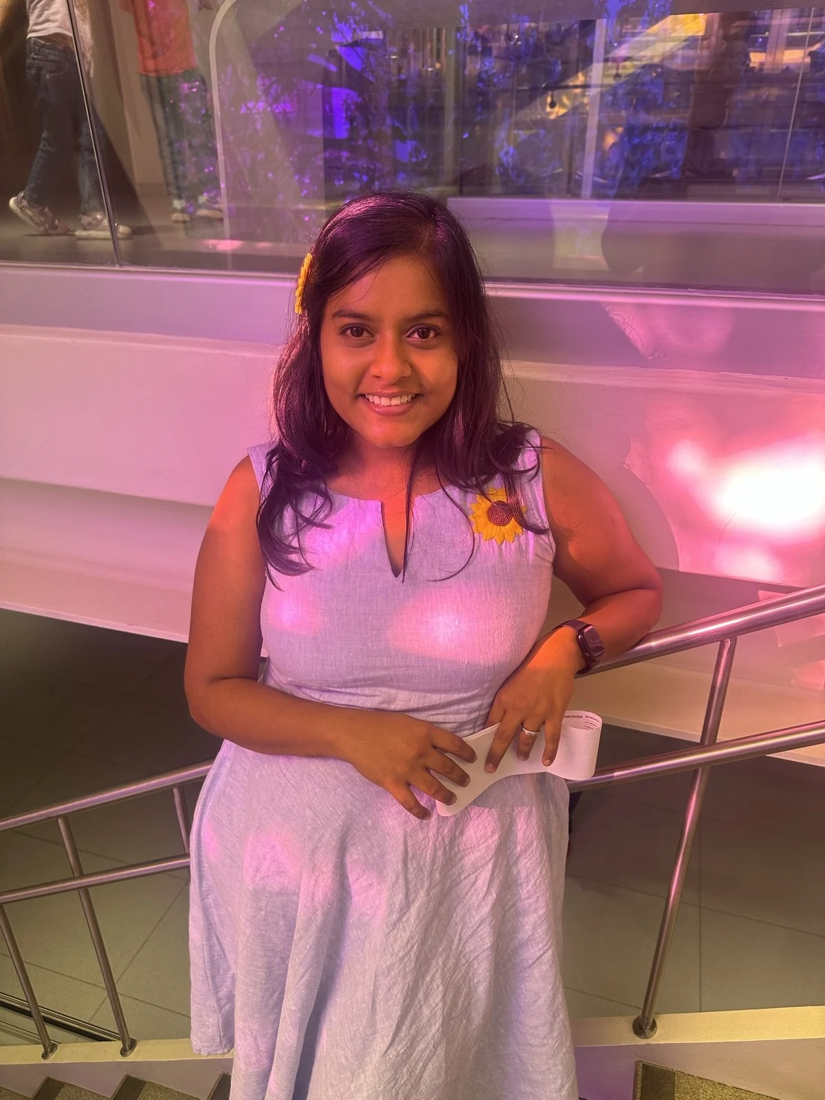 Premika smiling in a lavender dress with a sunflower pin.