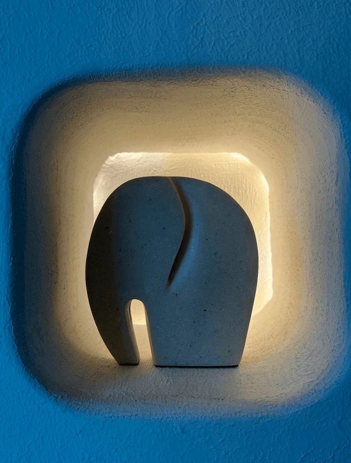 A warm-lit sculptural wall light against a blue wall.