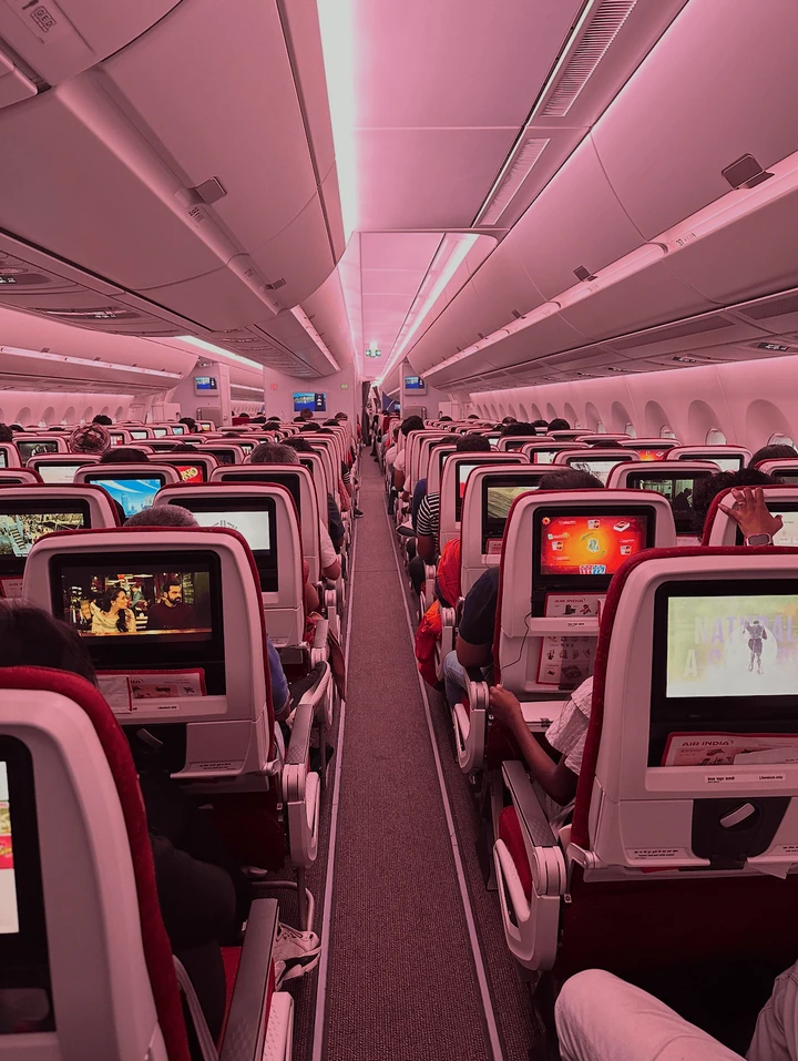 Rows of aeroplane seats under pink cabin lighting.