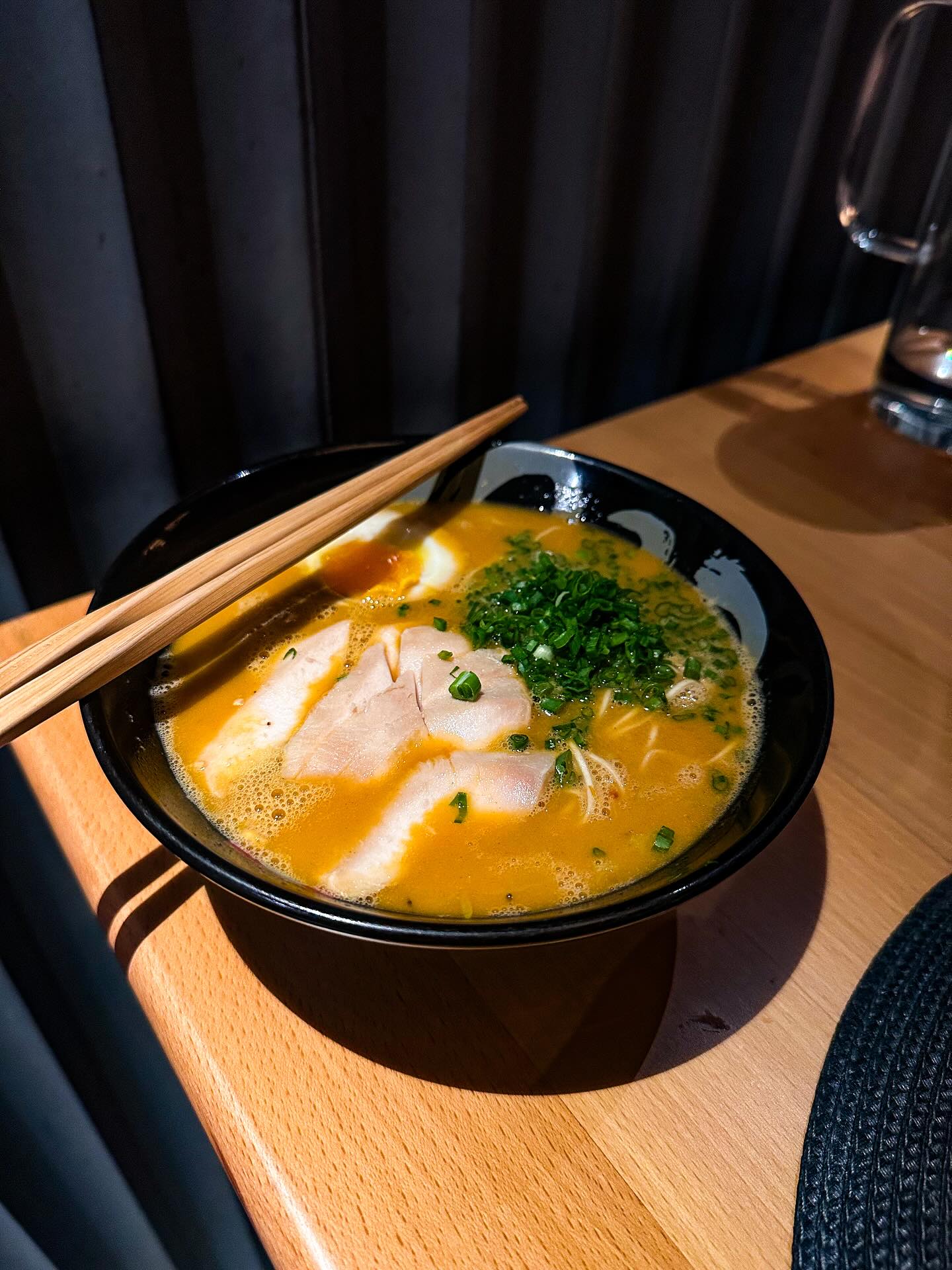 A bowl of noodles and chopsticks in a softly lit restaurant.