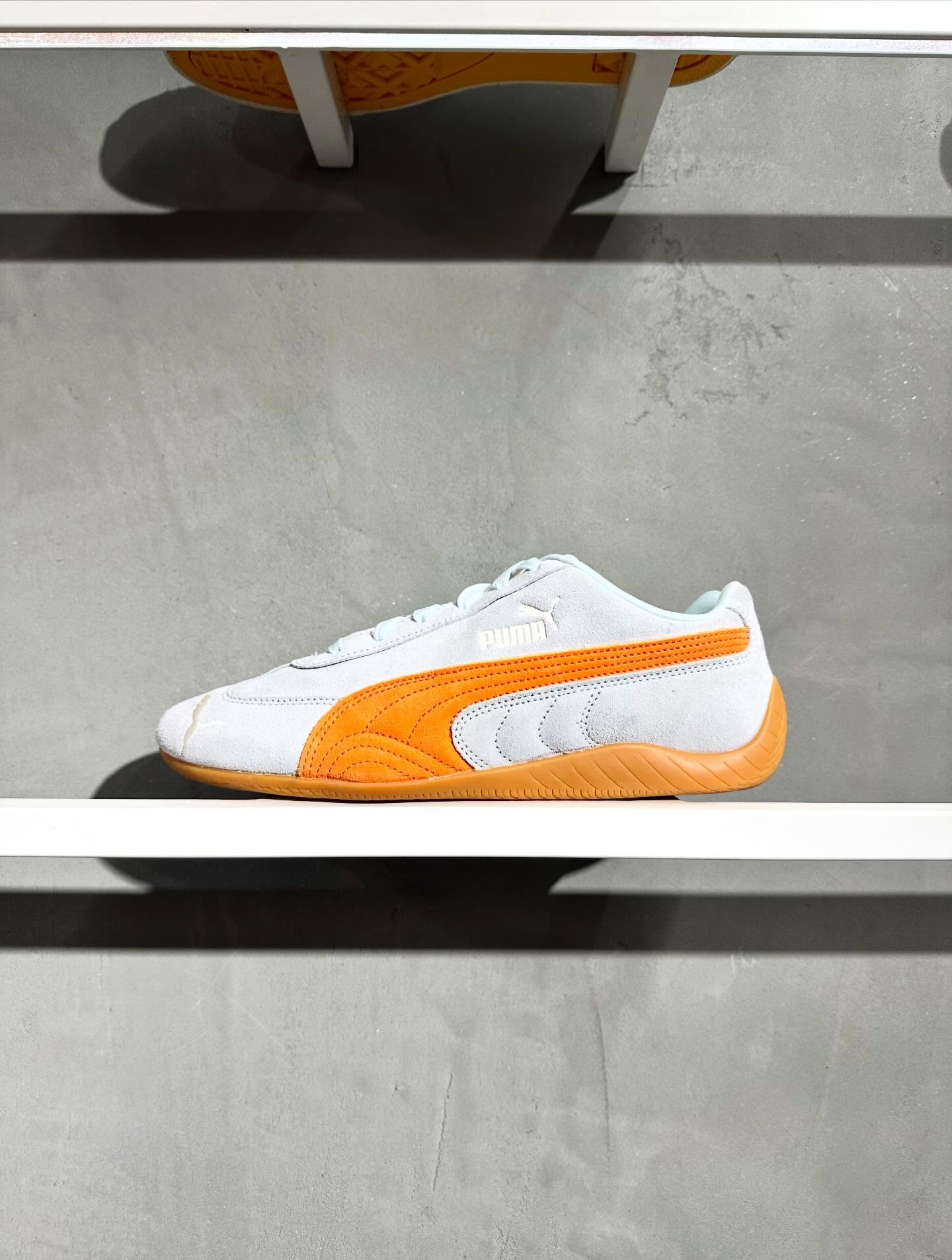 A white-and-orange sneaker on a sunlit display shelf with geometric shadows.