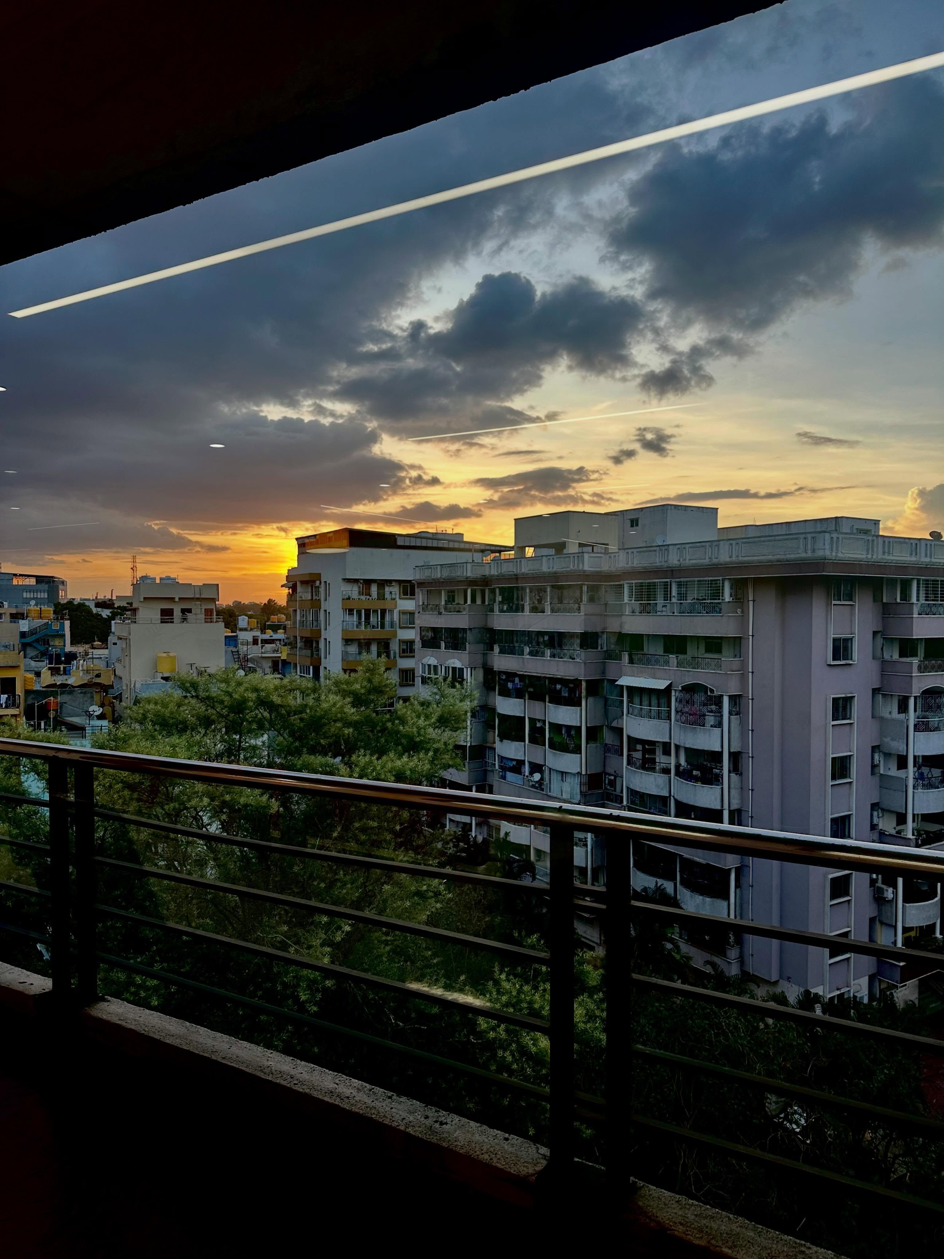 Sunset light breaking through dark clouds beyond an apartment balcony.