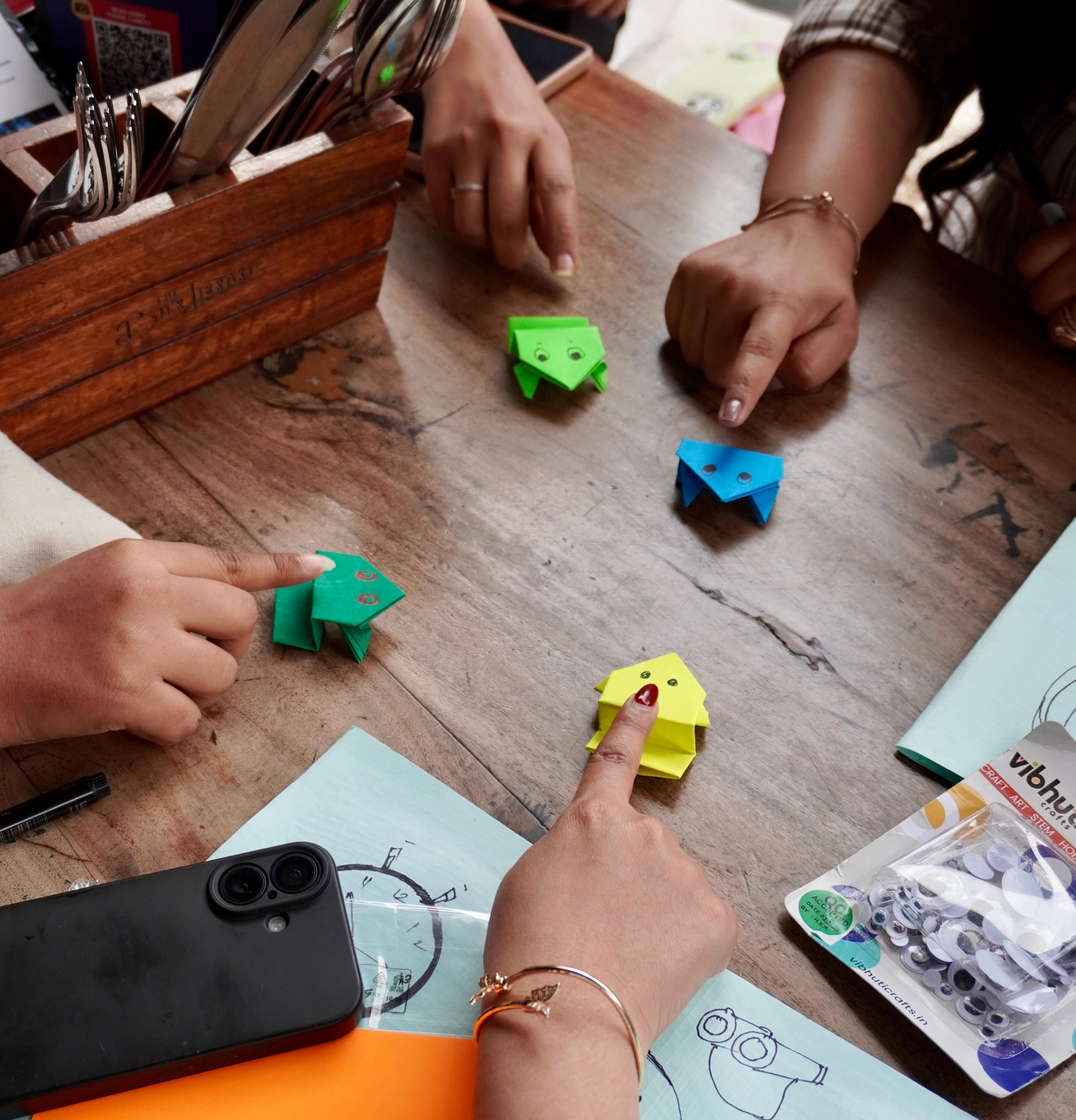 Friends playing with colorful folded paper pieces around a wooden table.