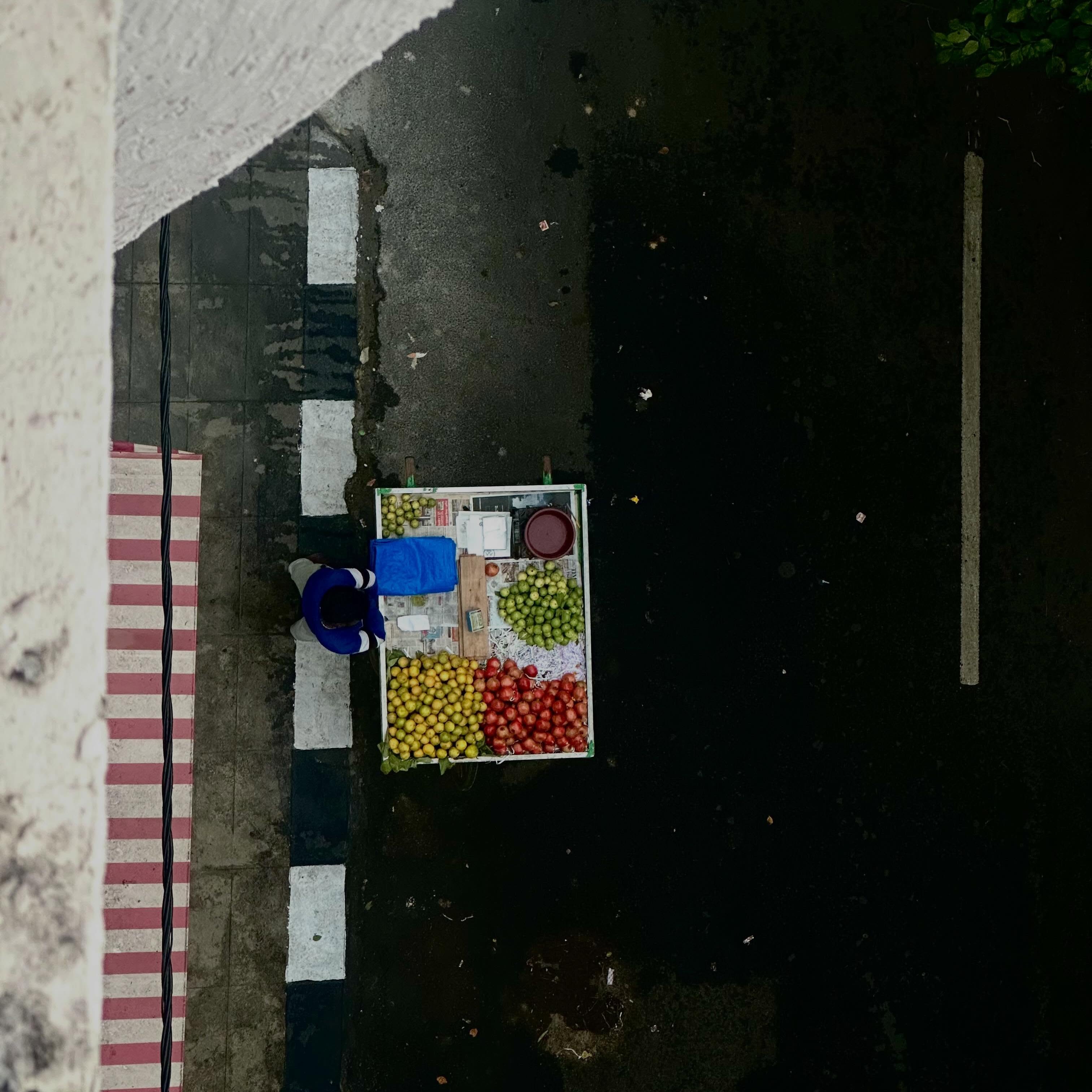 An overhead view of a fruit seller beside a striped pavement.
